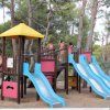 Un'area giochi per bambini con scivoli blu e una struttura in legno tra gli alberi.