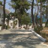 Viale tra alberi con edifici bianchi e vista sul mare.