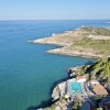 Vista aerea di una costa con mare azzurro, vegetazione e piscina.