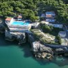 Un complesso con piscina situato su una scogliera circondata da alberi e mare blu.