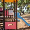 Un parco giochi con scivolo blu e strutture in legno tra gli alberi.