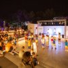 Persone assistono a uno spettacolo serale su un palco all'aperto.