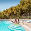 Persone rilassate a bordo piscina sotto gli alberi.