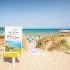 Spiaggia sabbiosa con ombrelloni e mare sullo sfondo.