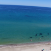 Spiaggia con mare calmo e limpido, persone che nuotano e ombrelloni colorati sulla sabbia.