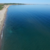Lunga spiaggia sabbiosa con mare tranquillo e diverse ombrelloni colorati sul bagnasciuga.