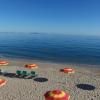 Spiaggia con ombrelloni rossi e gialli, mare calmo all'orizzonte.