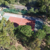 Campo da tennis con superficie rossa, circondato da alberi e una strada vicina.