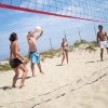 Quattro persone giocano a beach volley su una spiaggia sabbiosa sotto un cielo azzurro.