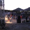 Persone assistono a uno spettacolo serale all'aperto, con sedie e palco illuminato.