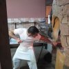 Un uomo in t-shirt bianca sforna una pizza da un forno in pietra.