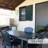 Veranda di una casa con tavolo nero e quattro sedie, cucina esterna e porta aperta.