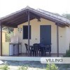 Una piccola casa con veranda, tavolo e sedie, immersa nel verde.