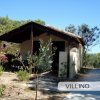 Un villino con veranda e sentiero, circondato da alberi e cespugli.