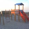 Area giochi all'aperto con scivolo e altalena sulla sabbia.