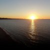 Tramonto sul mare con riflessi d'acqua e costa a sinistra.
