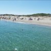 Spiaggia affollata con mare cristallino e bagnanti.