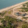 Vista aerea di una spiaggia con edifici esagonali e vegetazione, bordata da mare e camminamenti.