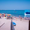 Spiaggia affollata con ombrelloni colorati e cartello 